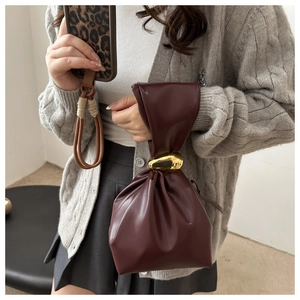 Detail of burgundy leather bucket bag with gold clasp shown on model with knit cardigan