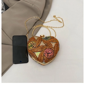 Macro view of heart-shaped evening bag with floral sequins and metal handle next to phone
