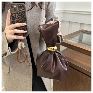 Detailed view of dark brown leather bucket bag featuring gold metal ring handle and pleats