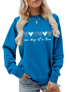 Dettaglio felpa blu con grafiche a cuore colorate e testo one day at a time