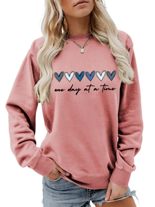 Dettaglio dei cuori blu e testo One Day at a Time sulla felpa rosa polvere da donna