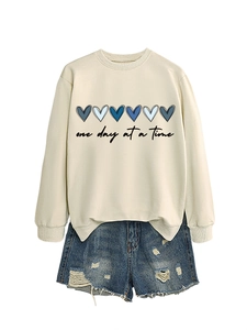 Dettaglio della felpa crema con cuori blu e pantaloncini in denim consumati