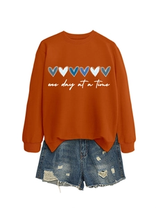 Dettaglio della felpa arancione con cuori blu e scritta One Day At A Time