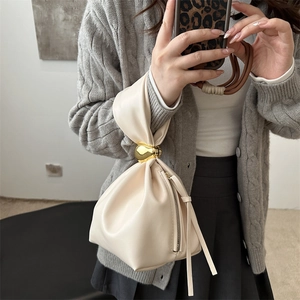 Chic beige pleated bucket bag with gold metal ball handle held by a model in mirror selfie