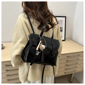 Rear view of model wearing black glossy leather backpack with baseball charm detail