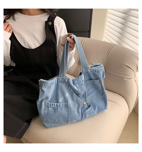 Close-up of light blue denim tote bag with front pocket and rivet detailing on a sofa