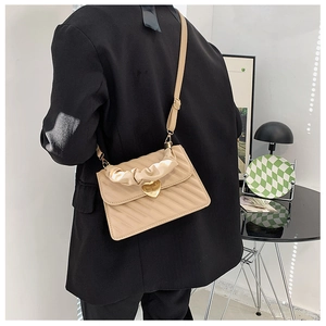 Bolso acolchado beige con cierre de corazón y asa fruncida sobre un blazer negro