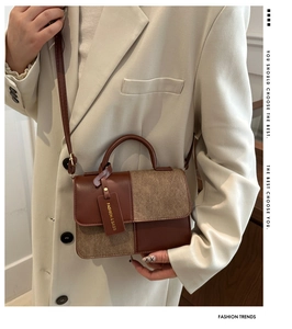 Detail van een bruine leren en beige stoffen crossbodytas op een crèmekleurige blazer