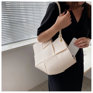 Detail of white woven leather tote showing wide strips and gold hardware on the strap
