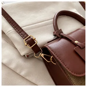 Detail of adjustable golden buckle and lobster clasp on brown leather shoulder bag