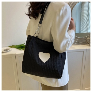 Primer plano del bolso tote negro texturizado con parche de corazón blanco y cadena plata