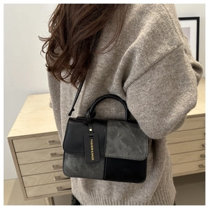 Detail van minimalistische tas met kleurblokken van grijs suède en zwart lederen stiksels
