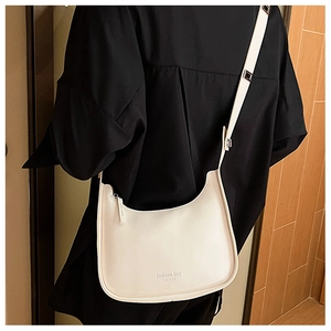 Detail of white leather crescent bag with fashion bag text worn on black outfit