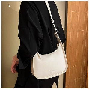 Detailed side view of off-white half-moon shoulder bag worn by model in a cozy room