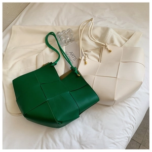 Detail of large woven leather tote bags in green and beige with slim shoulder straps