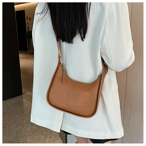 Close-up of brown leather half-moon shoulder bag worn with a white blazer for fashion