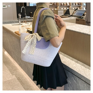 Detail of woven straw tote bag with lace bow and purple cylindrical braided handles
