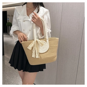 Close-up of beige woven straw tote bag featuring white lace bow and rope handle detail