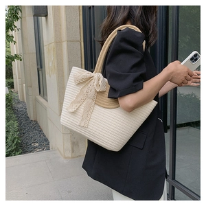 Detail of cream straw tote bag featuring delicate lace bow and woven shoulder strap
