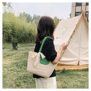 Detailed woven straw tote bag featuring a green handle and a delicate lace bow accent