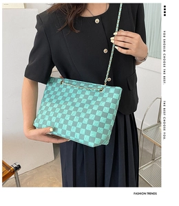 Detail of teal checkerboard shoulder bag featuring textured pattern and gold chain strap