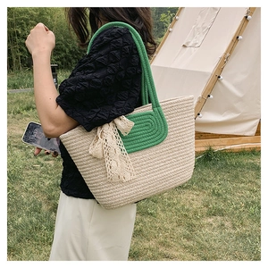 Detail of hand-woven straw tote bag with green rope handles and elegant beige lace ribbon bow