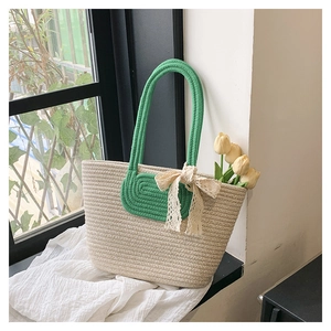 Detail of woven straw tote bag with green handles and a decorative beige lace bow