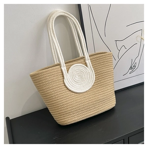 Detail of woven straw tote bag featuring white rope handles and swirl pattern decoration