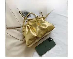 Size comparison of golden dumpling bag with an iPhone on soft beige fabric