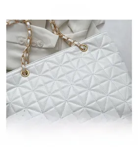 Detail of white quilted tote bag with golden metal chain strap and luxury stitching