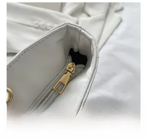 Detail of a white quilted tote bag featuring a polished gold zipper and chain strap