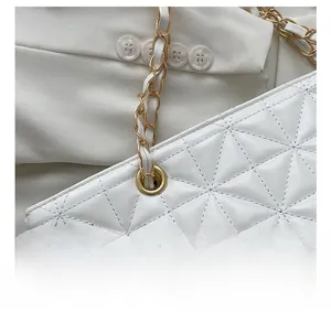 Detailed macro view of white quilted texture with woven gold metal chain strap on a tote bag
