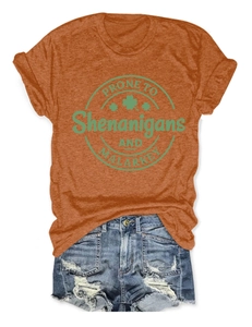 Flat lay of an orange crew neck tee with clover print and distressed denim shorts