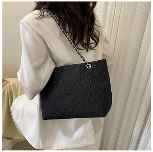 Detail of black tote bag featuring textured bubble fabric and metal chain strap