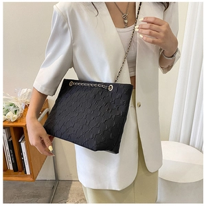 Close-up of black quilted tote bag with gold chain strap on a model wearing white blazer