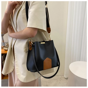 Detail einer schicken Bucket Bag in Schwarz mit braunem Rand und breitem Streifengurt