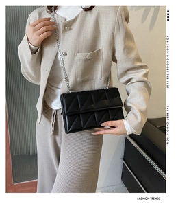 Close-up of black quilted crossbody bag with silver chain strap on tweed jacket