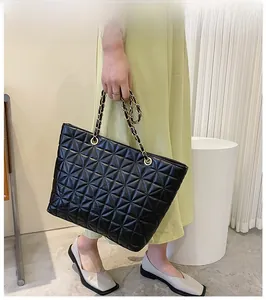 Detail of black quilted tote bag featuring gold chain strap and geometric rhombus pattern