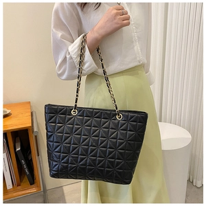 Detail of black quilted tote bag with gold chain strap on model in minimalist setting