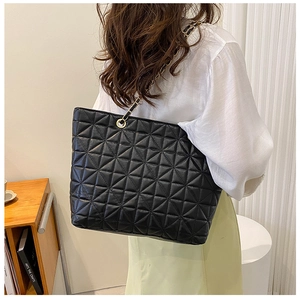 Detail of a large black quilted tote bag with chain strap worn over the shoulder