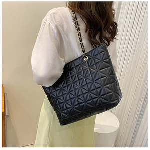 Detail of black quilted star pattern tote bag with gold chain strap on model