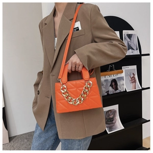 Gros plan d'un sac matelassé orange avec chaîne dorée épaisse porté par un mannequin