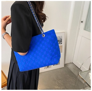 Detail of Klein Blue quilted tote bag with metal chain strap worn by a female model