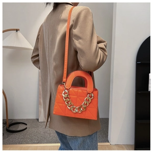 Sac bandoulière matelassé orange avec chaîne dorée porté par un mannequin chic