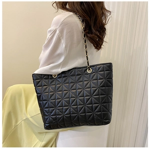 Detail of black quilted tote bag with gold chain strap worn by a female model