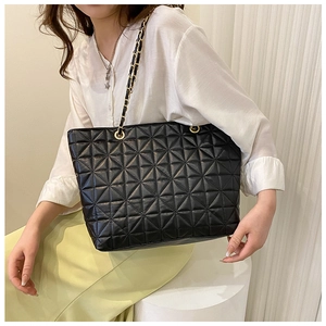 Detail of black quilted leather tote bag with elegant gold-tone chain strap on shoulder