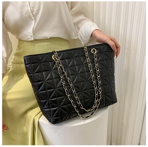 Detail of black quilted tote bag with geometric texture and gold chain straps