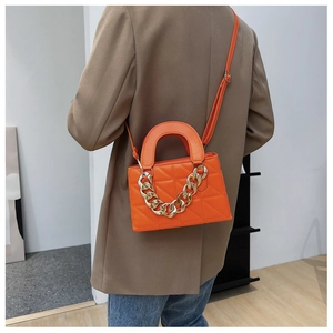 Détail d'un sac à main matelassé orange avec chaîne dorée et poignée supérieure