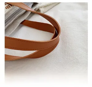 Detail of reinforced brown faux leather handles and zipper on a canvas tote bag