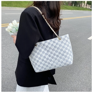 Blue and white checkerboard tote bag with golden chain strap in an outdoor lifestyle setting